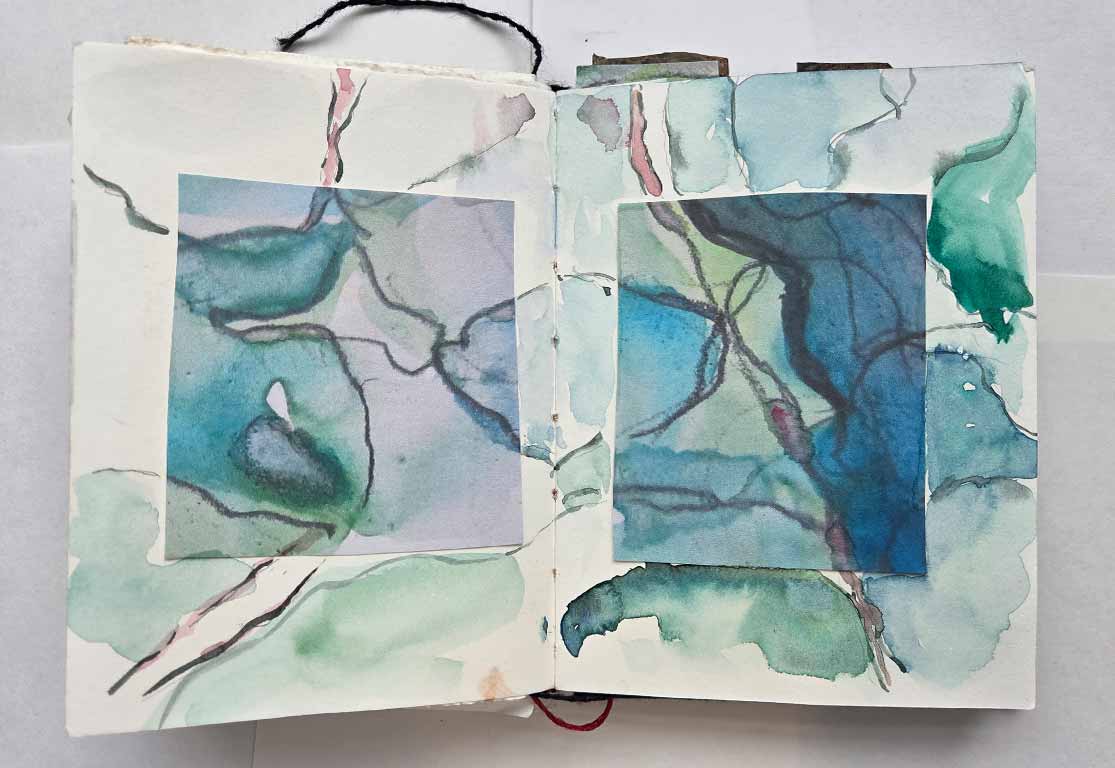 Open sketchbook with abstract watercolor paintings in blue and green hues on both pages.