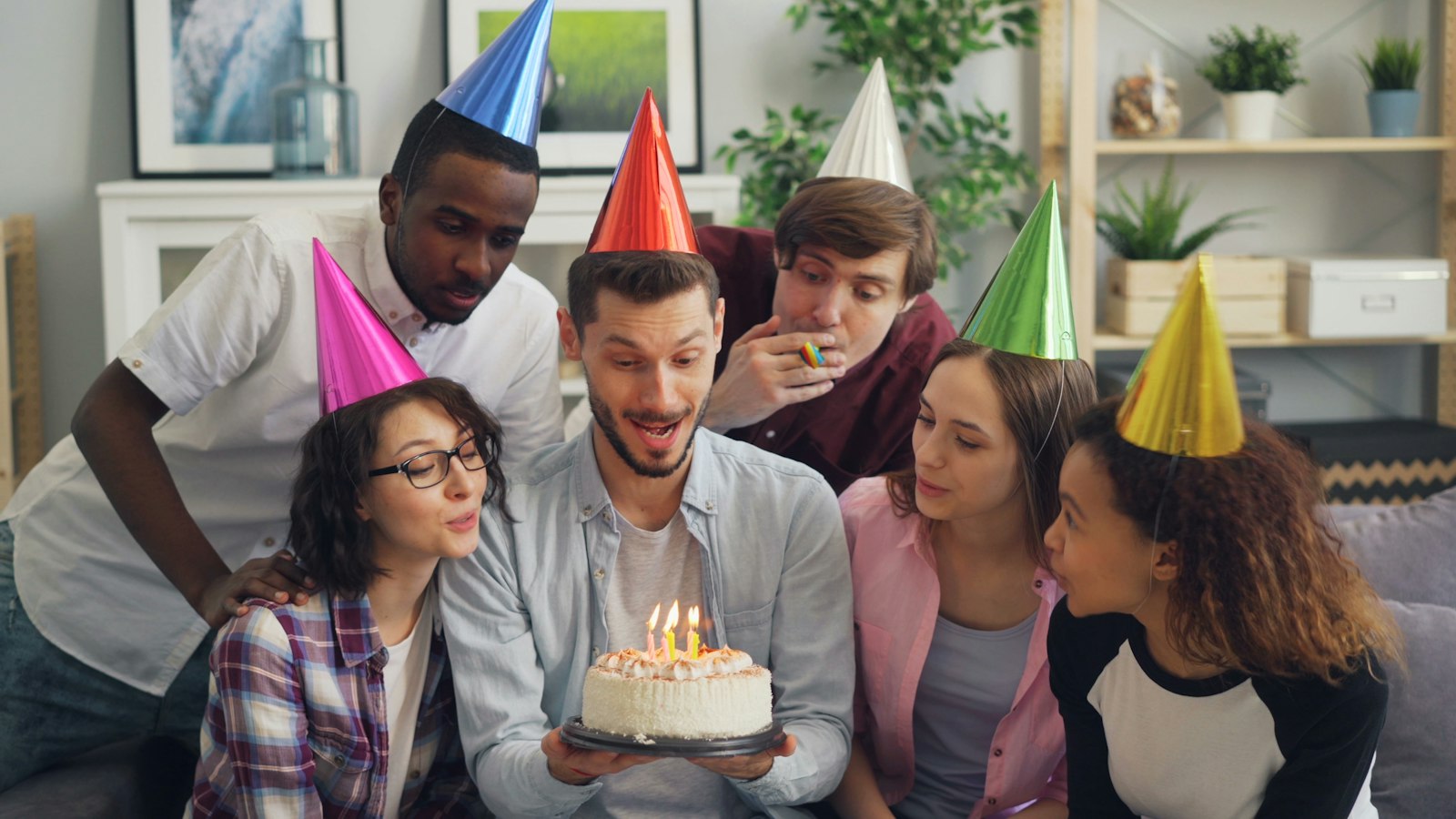 Friends in party hats gathered around a birthday cake with candles