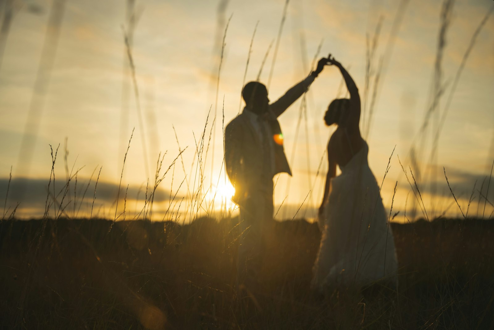 A bride and groom dancing in a field at sunset