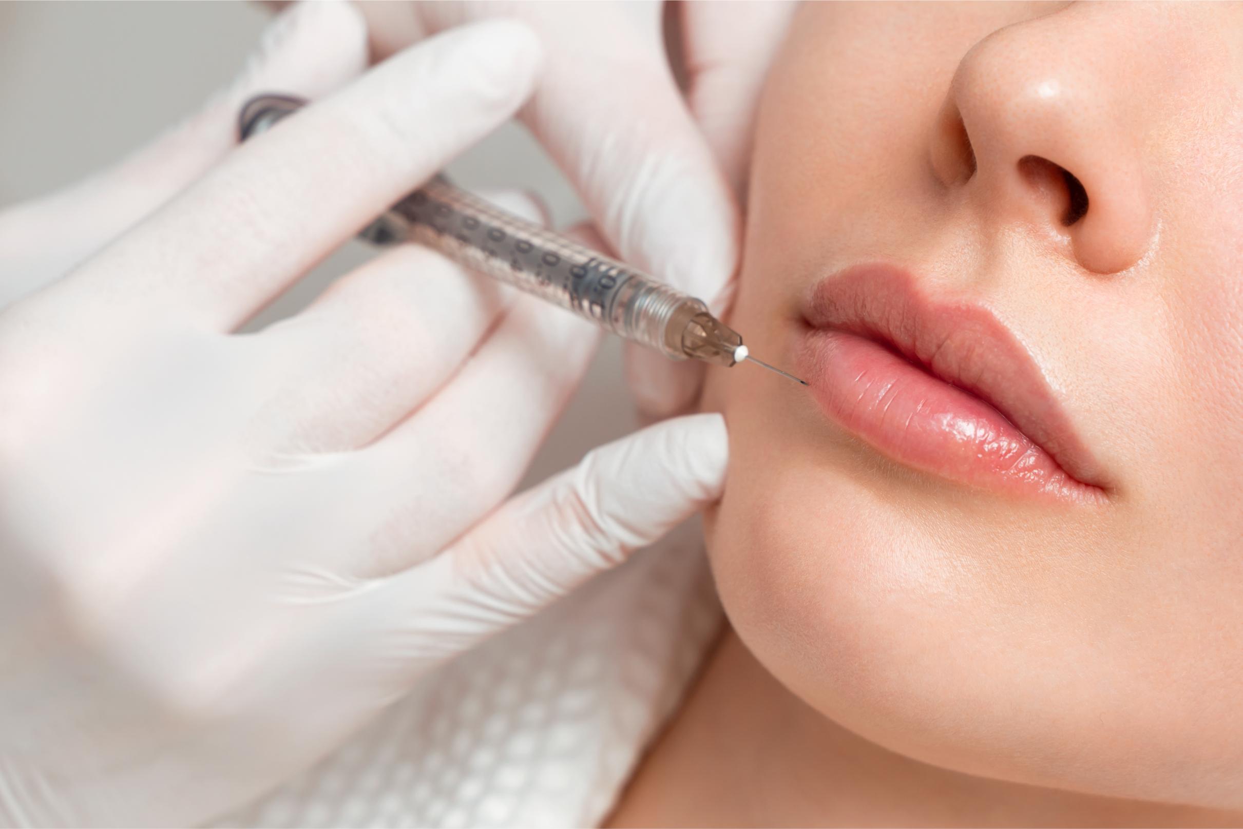 Woman with closed eyes receiving a cosmetic injection in her forehead from a gloved professional.