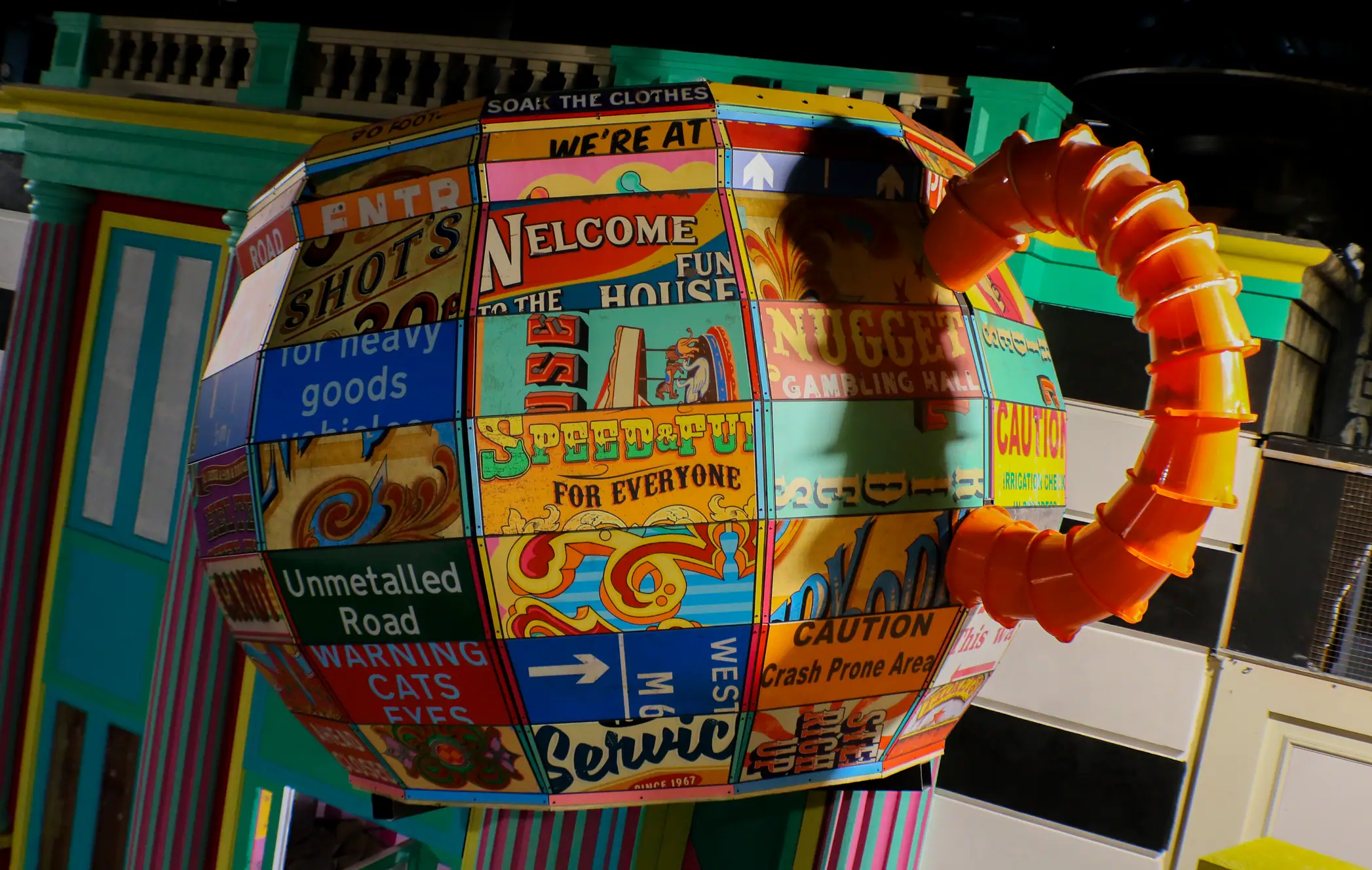 Colorful spherical object made of various vintage signs with an orange segmented tube attached.