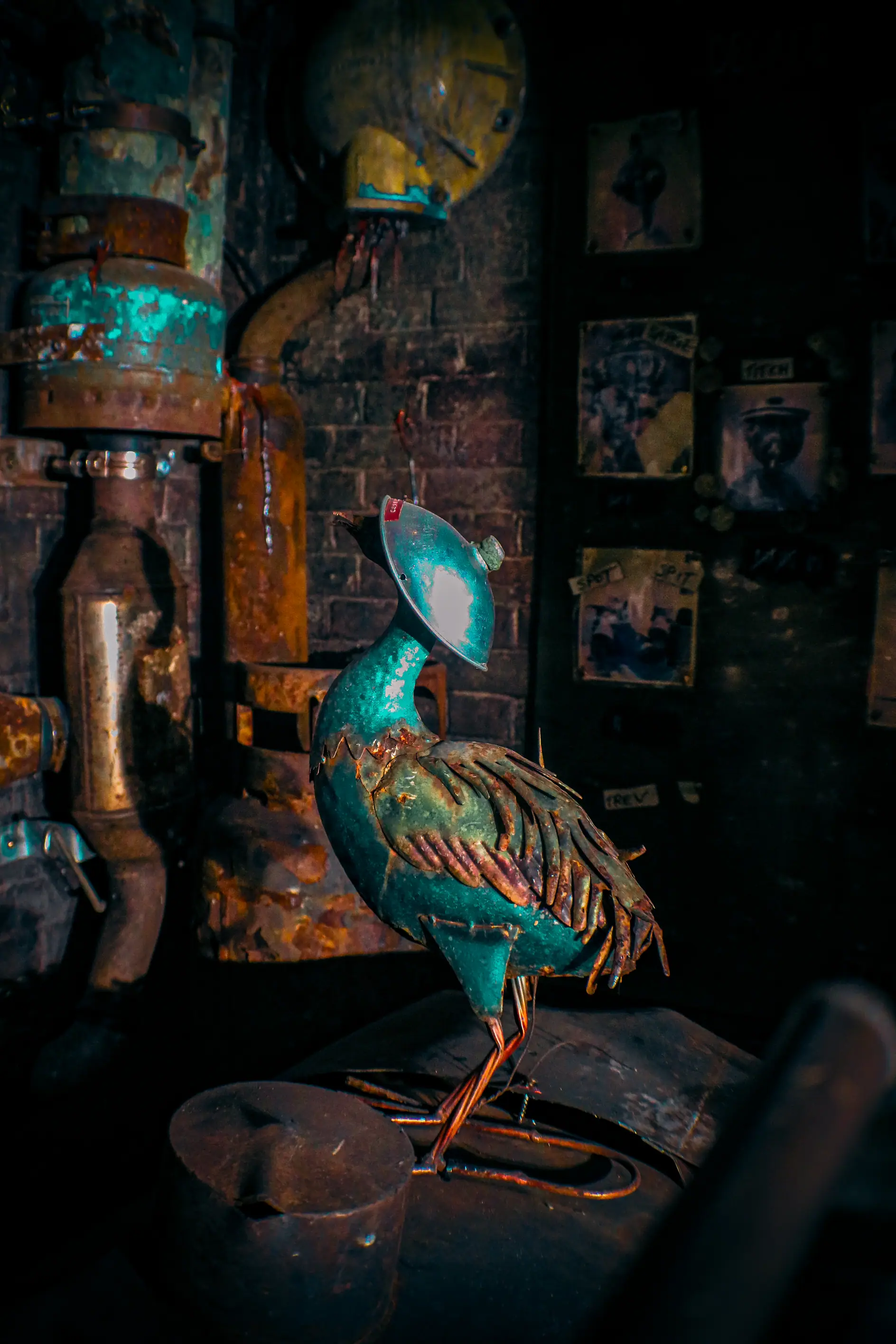 Rusty metal bird sculpture perched on machinery in an industrial setting with dark background.