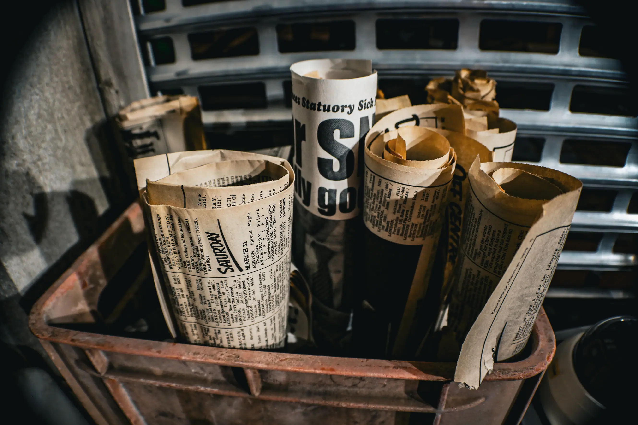Rolled-up newspapers tightly packed vertically inside a rusty metal crate.