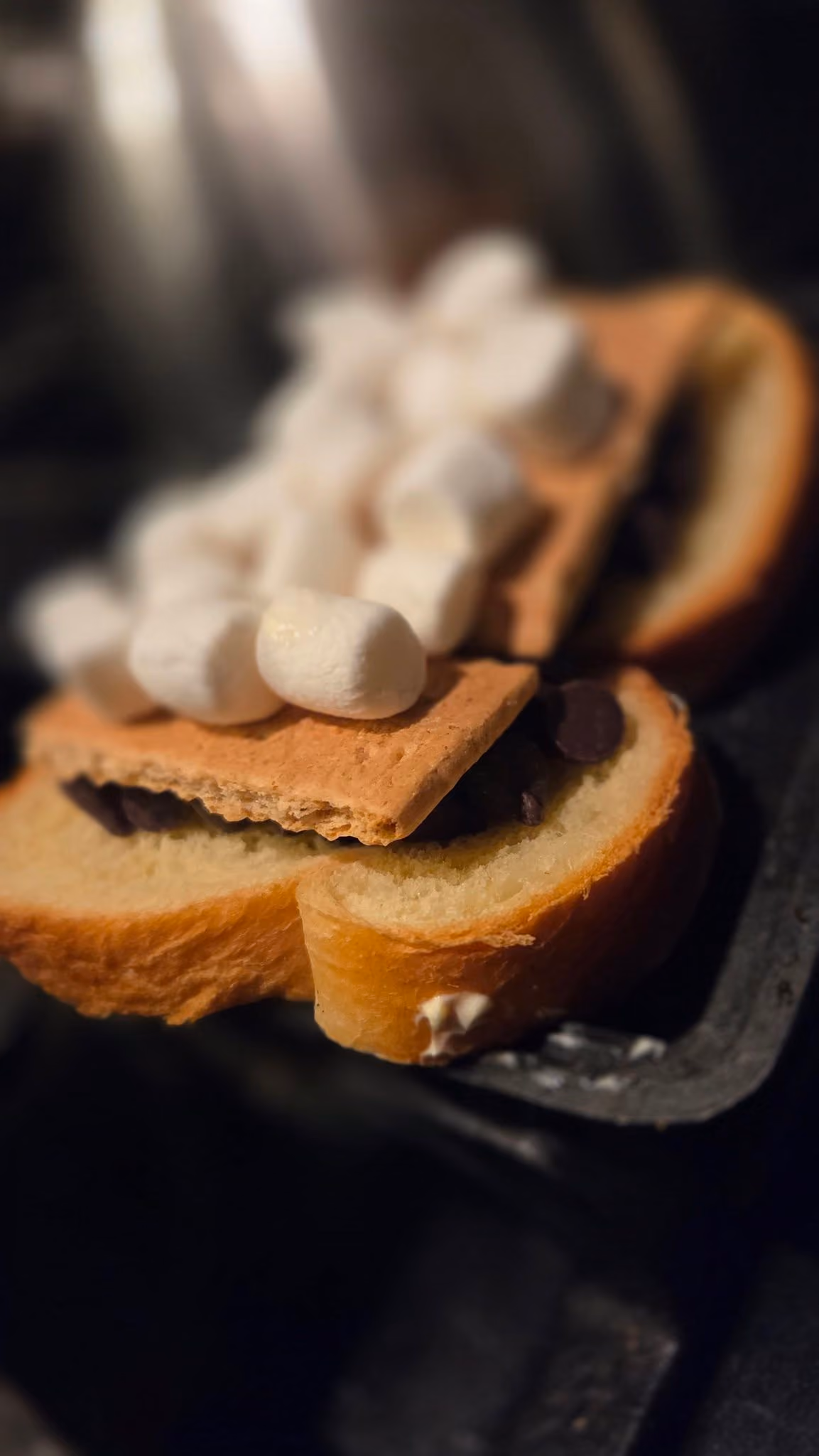 Open sandwich with graham cracker, chocolate pieces, and small marshmallows, in warm lighting.
