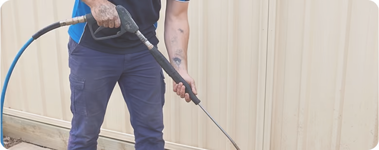 Person wearing blue pants using a pressure washer to clean a concrete surface.