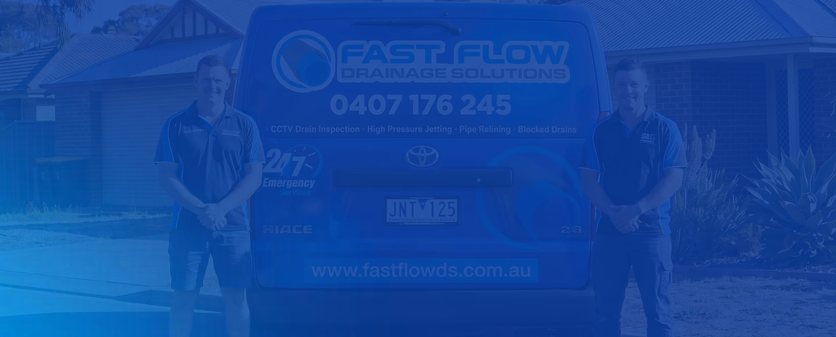 Two men in uniform standing beside a van advertising Fast Flow Drainage Solutions with contact info.