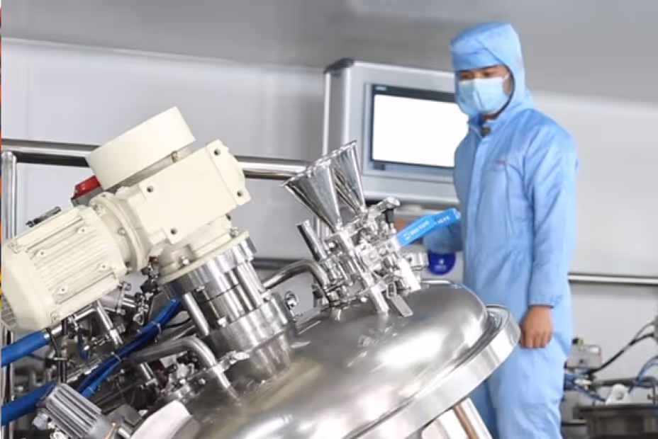 Person in blauer Schutzkleidung und Maske bedient industriellen Edelstahltank in einer sauberen Produktionsanlage.
