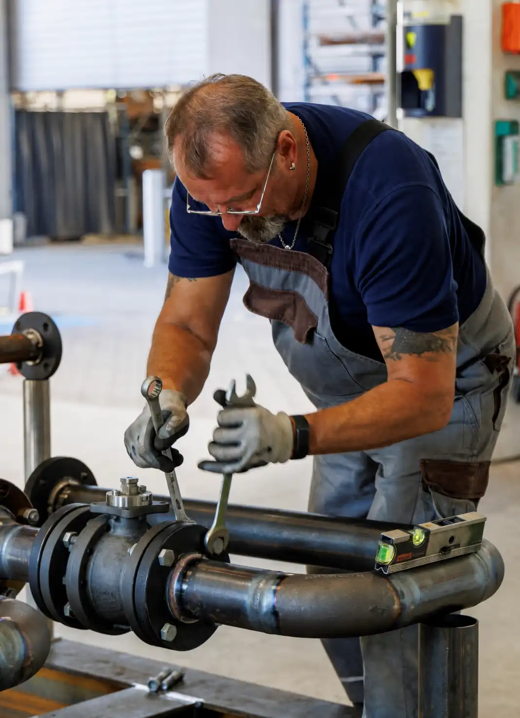Handwerker mit Handschuhen verwendet zwei Schraubenschlüssel, um ein Metallrohr in einer Werkstatt zu justieren.
