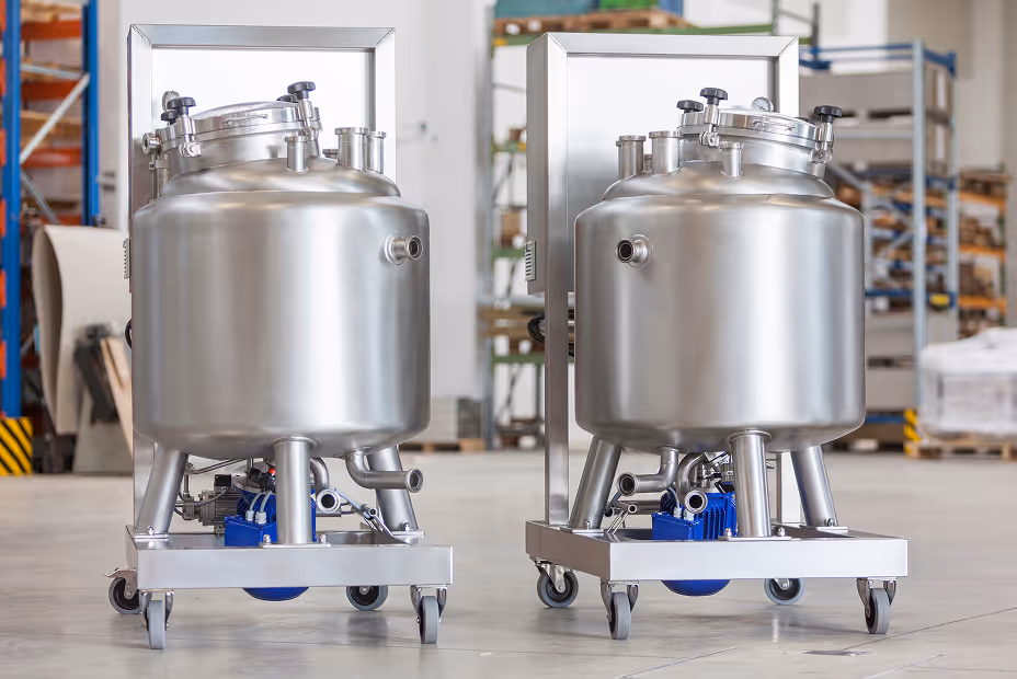 Zwei Edelstahlbehälter mit Ventilen und Pumpen auf Rollen in einer industriellen Lagerhalle.