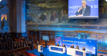 Conférence dans une grande salle ornée avec un écran affichant un intervenant au sommet européen ETI.