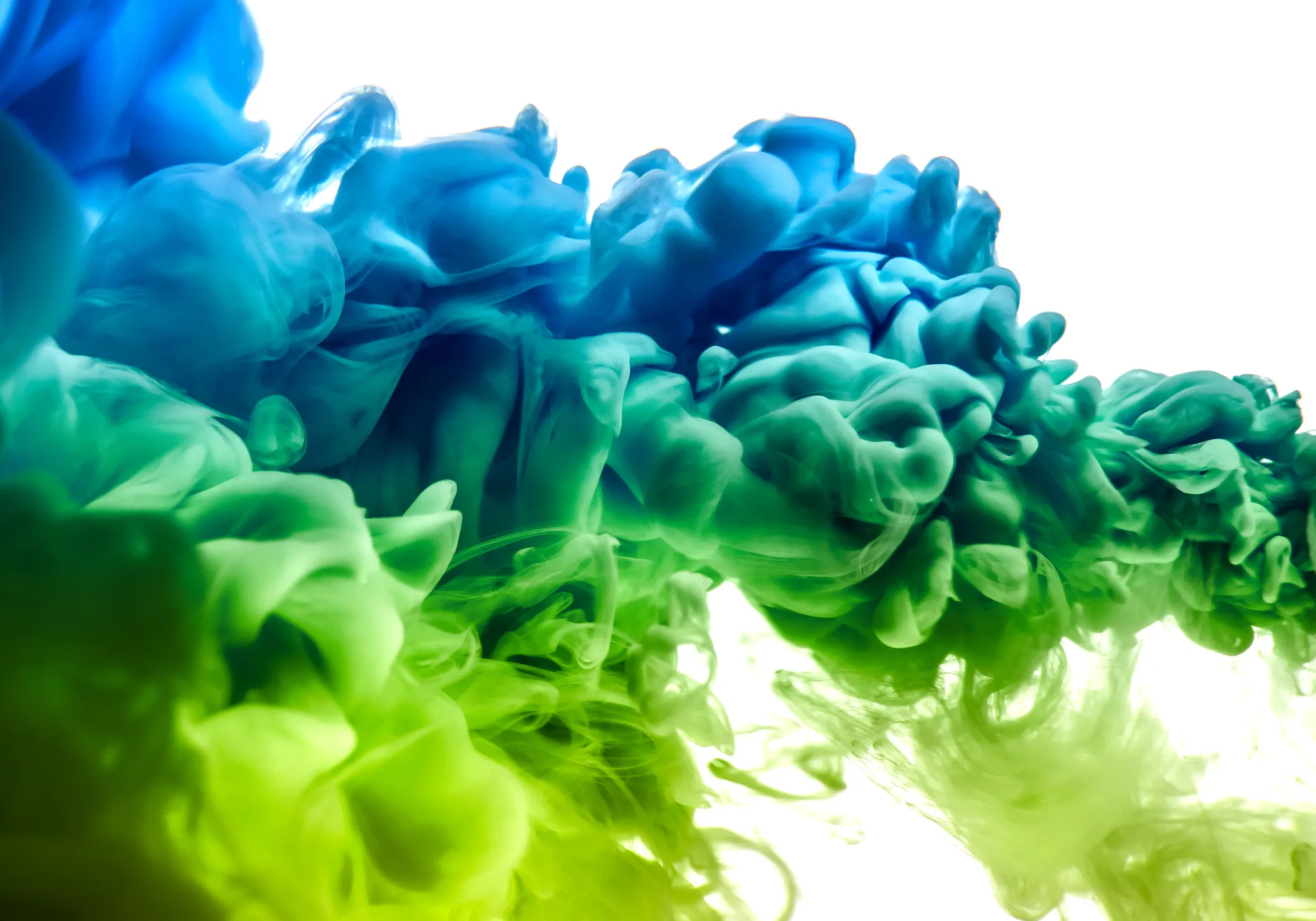 Swirling plumes of blue and green ink mixing in water against a white background.