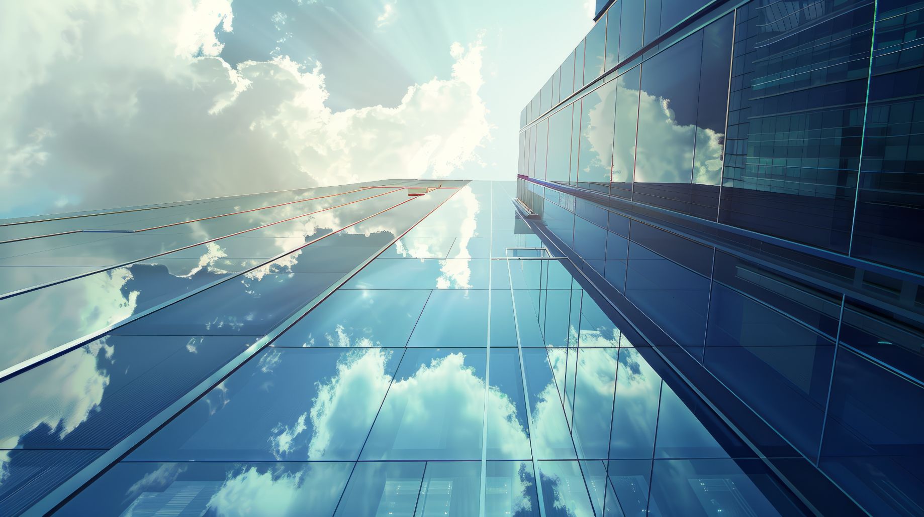 Upward view of modern skyscrapers with glass facades reflecting a blue sky with white clouds.