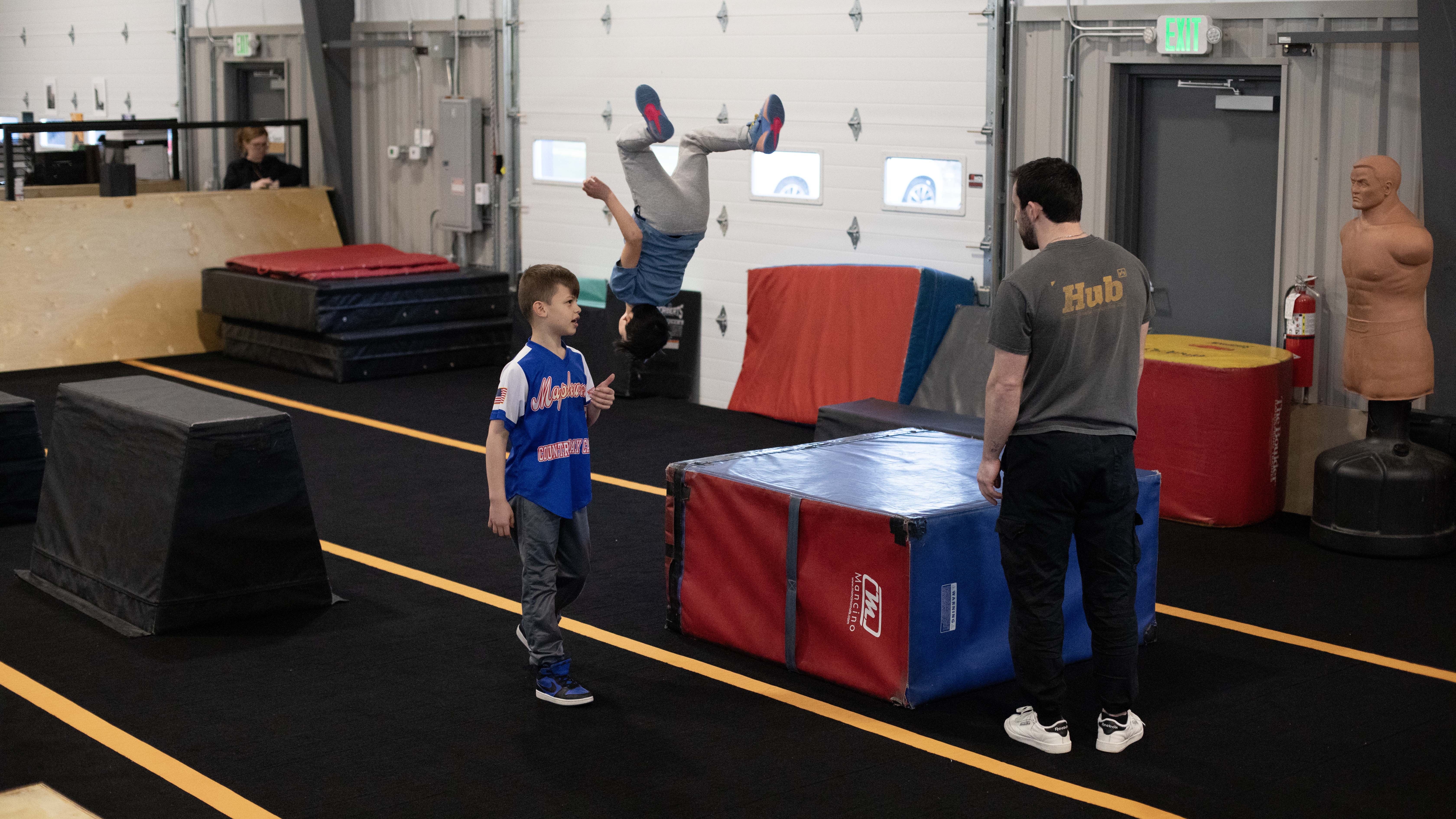 An athlete flips across the Norfolk floor while a coach watches