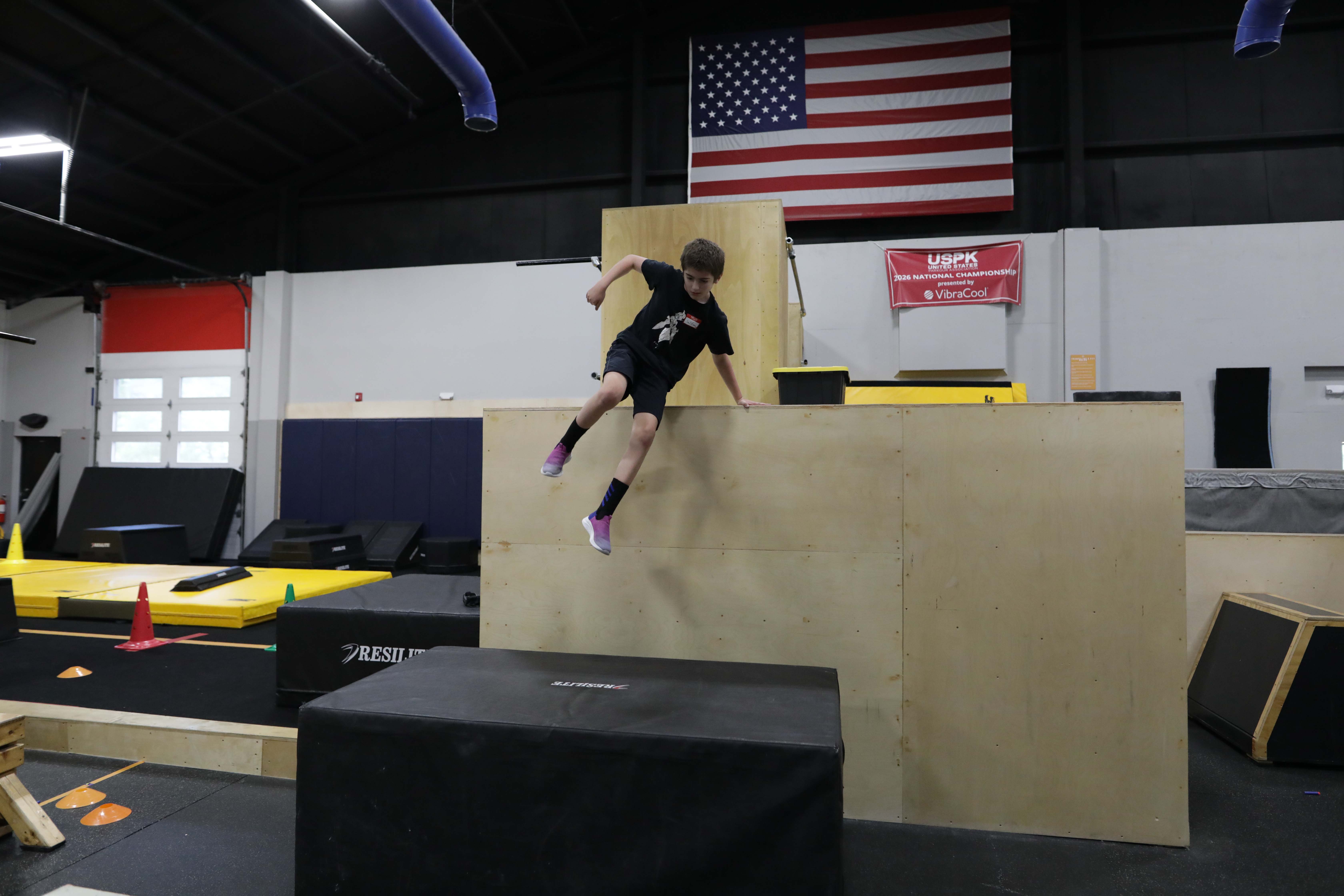 Youth athlete jumping from a tall wooden obstacle at HUB Parkour Sudbury.