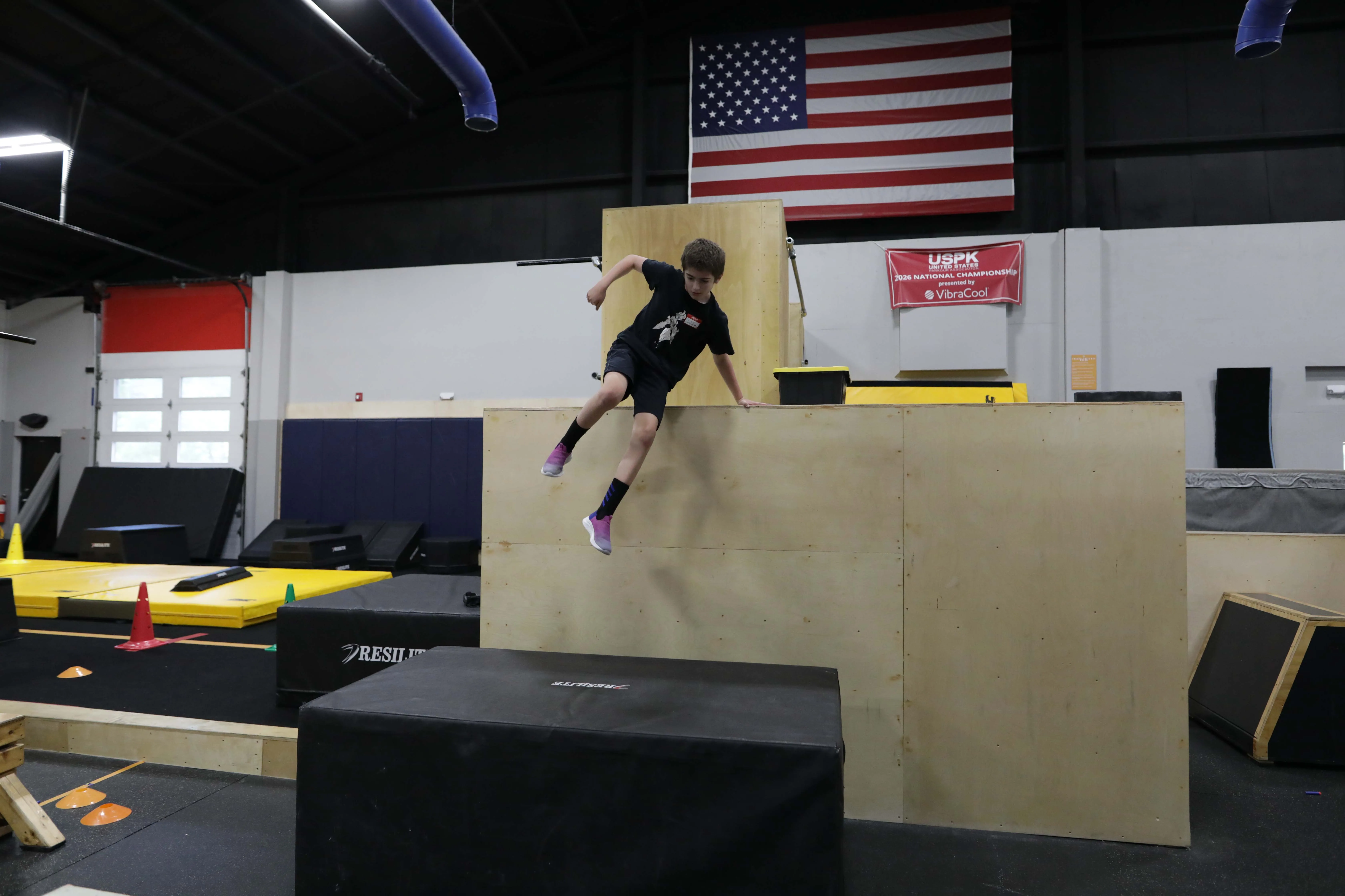 Youth athlete jumping from a tall wooden obstacle at HUB Parkour Sudbury.