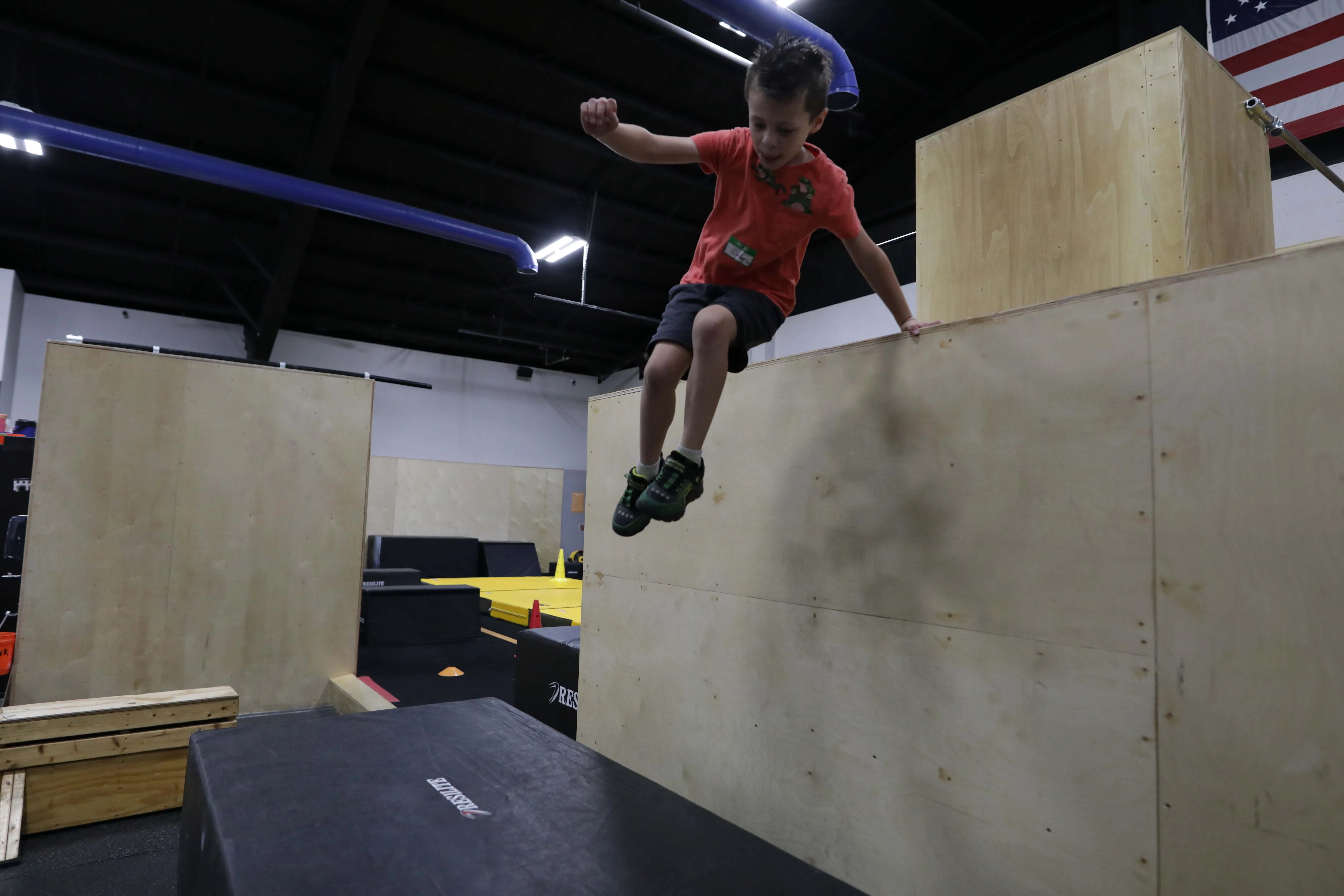 Young camper jumping down from a wooden parkour wall onto a padded mat.
