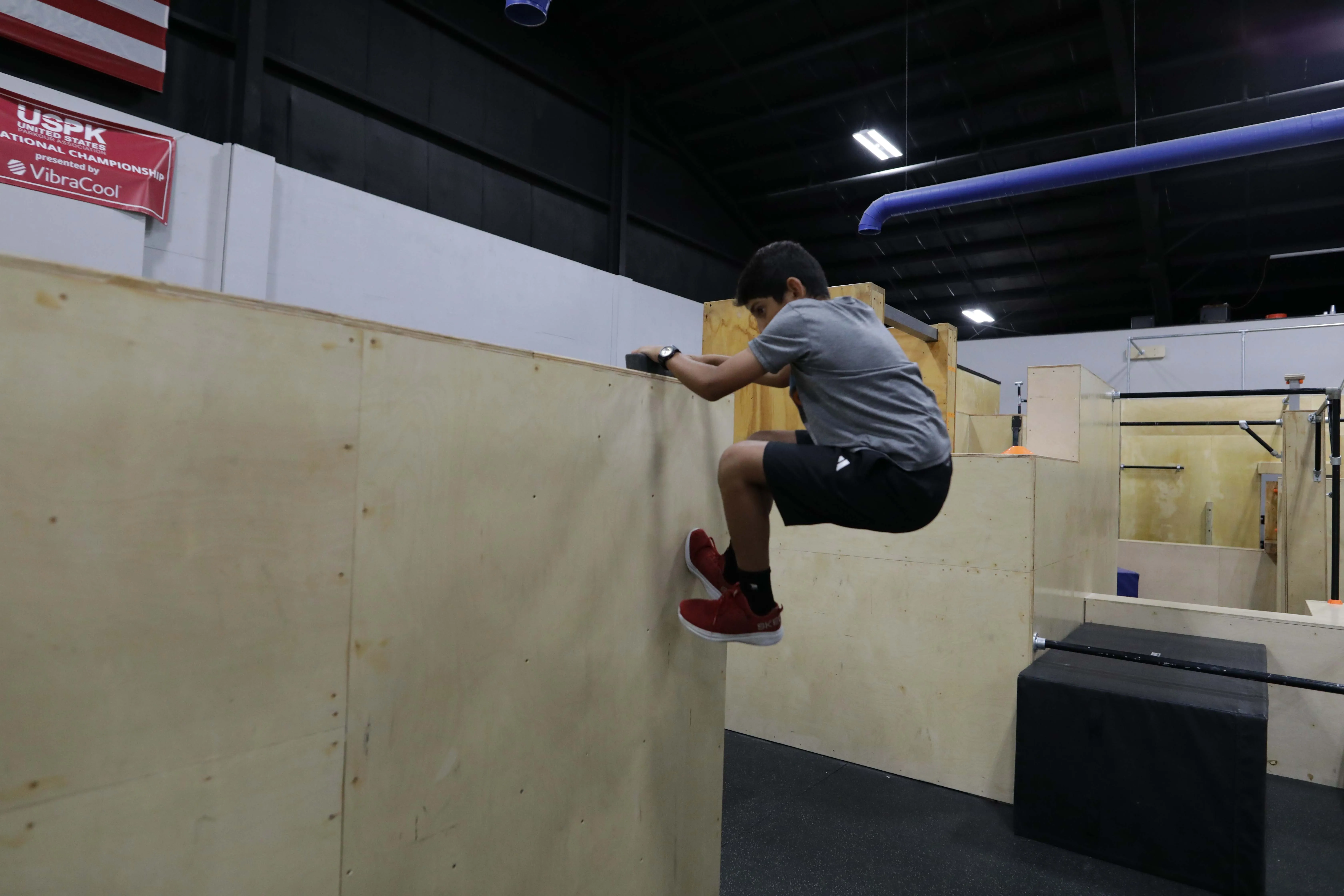 Young athlete climbing over a wooden parkour wall during CampHUB.