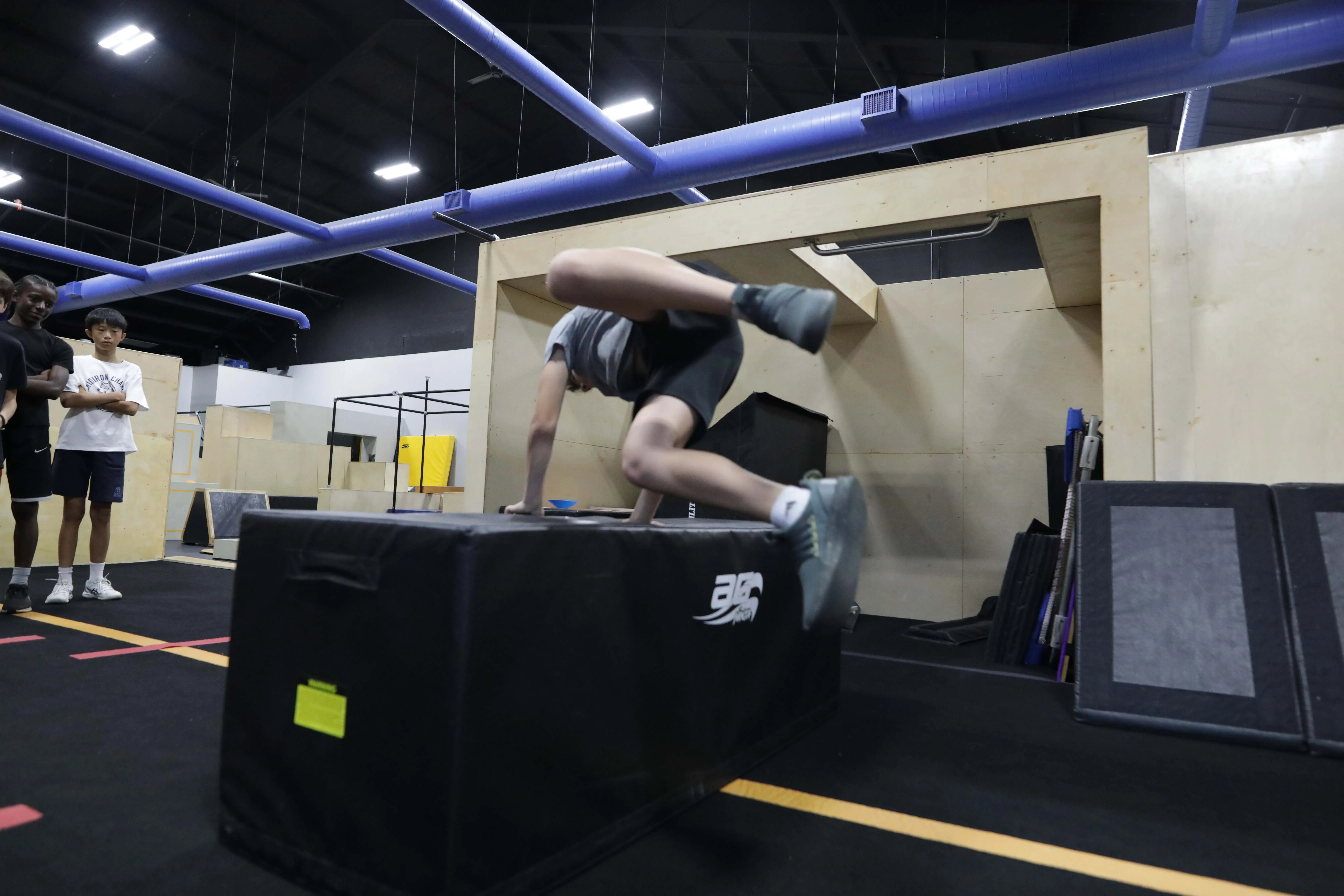 Camper vaulting over a padded parkour block while other athletes watch.