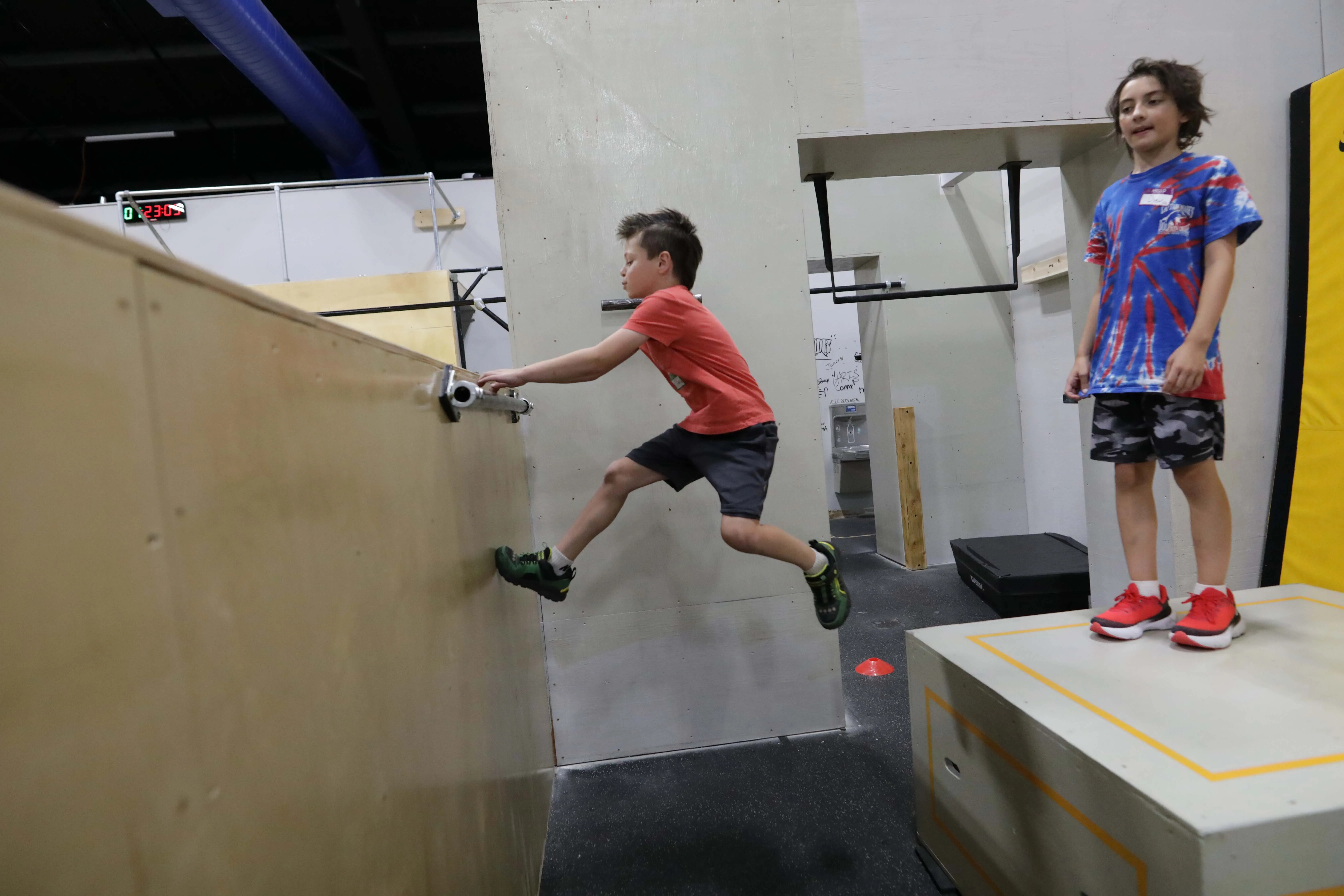 A kid grins on the box while a friend takes his turn at the wall