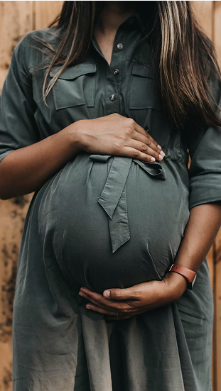 Close-up of a pregnant woman wearing a gray dress holding her belly with both hands.