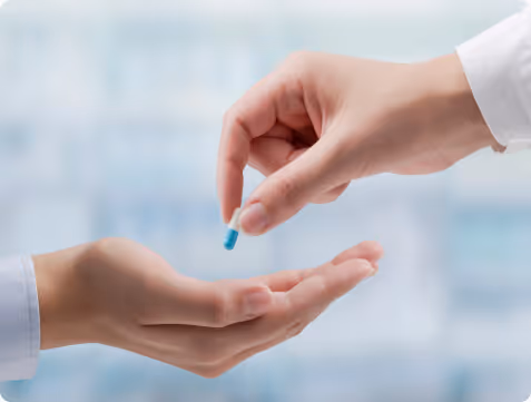 A close-up of two hands, one hand holding a blue and white capsule pill and giving it to the other open hand.