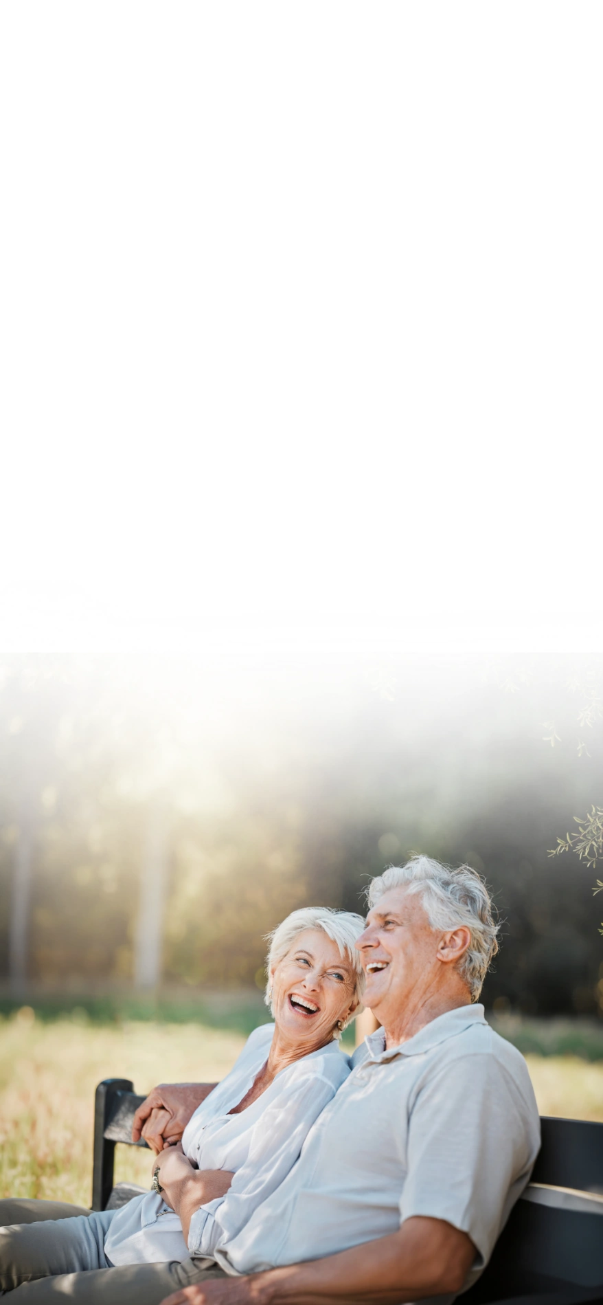 Smiling elderly couple sitting close together on a park bench, enjoying a sunny day outdoors.