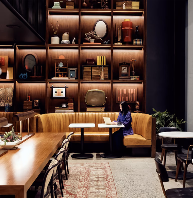 Woman working on laptop at table inside cozy cafe with vintage decor and bookshelf wall.