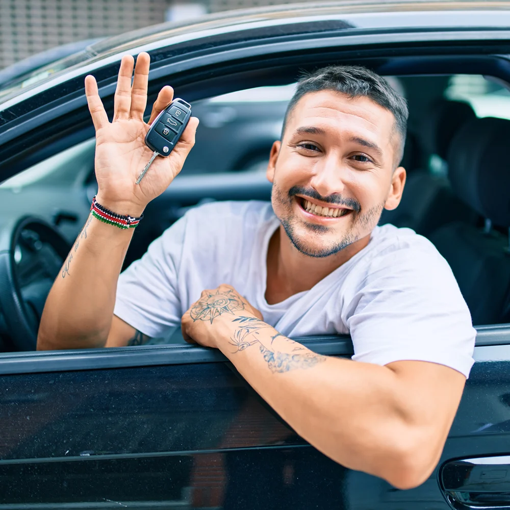 Smiling man with tattoos holding car keys while sitting in driver's seat of a black car because of Reentry Wheels.