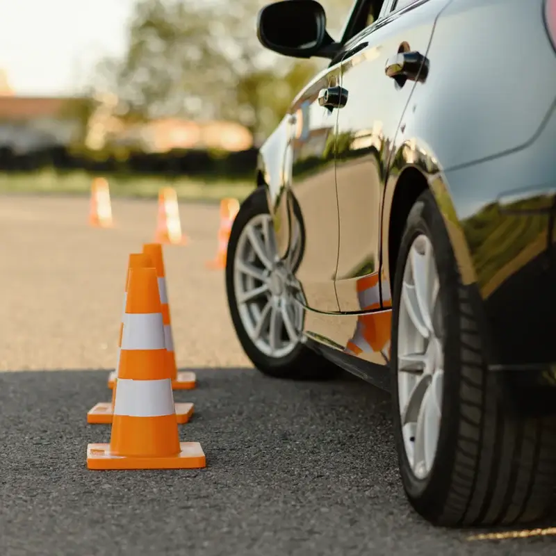 Black car parked next to a line of orange traffic cones on pavement during daylight during defensive driving class.