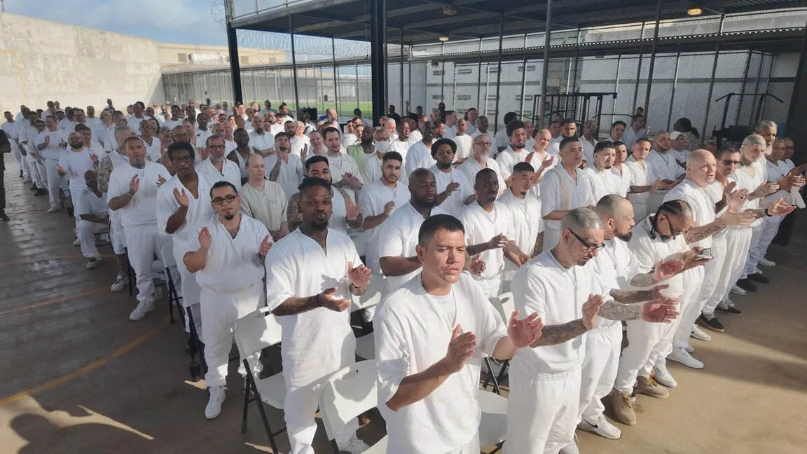 Rows of inmates in white clapping at outdoor prison service