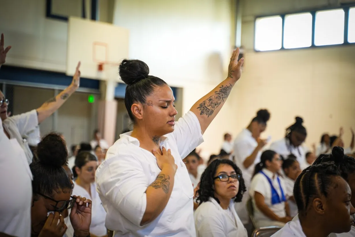 Woman raising hands in worship inside prison gymnasium