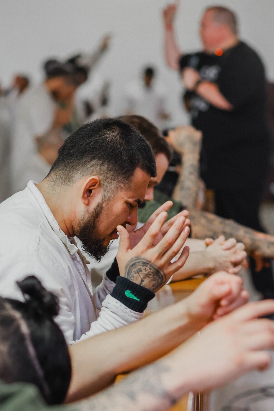 Man kneeling in prayer with hands clasped at prison chapel altar