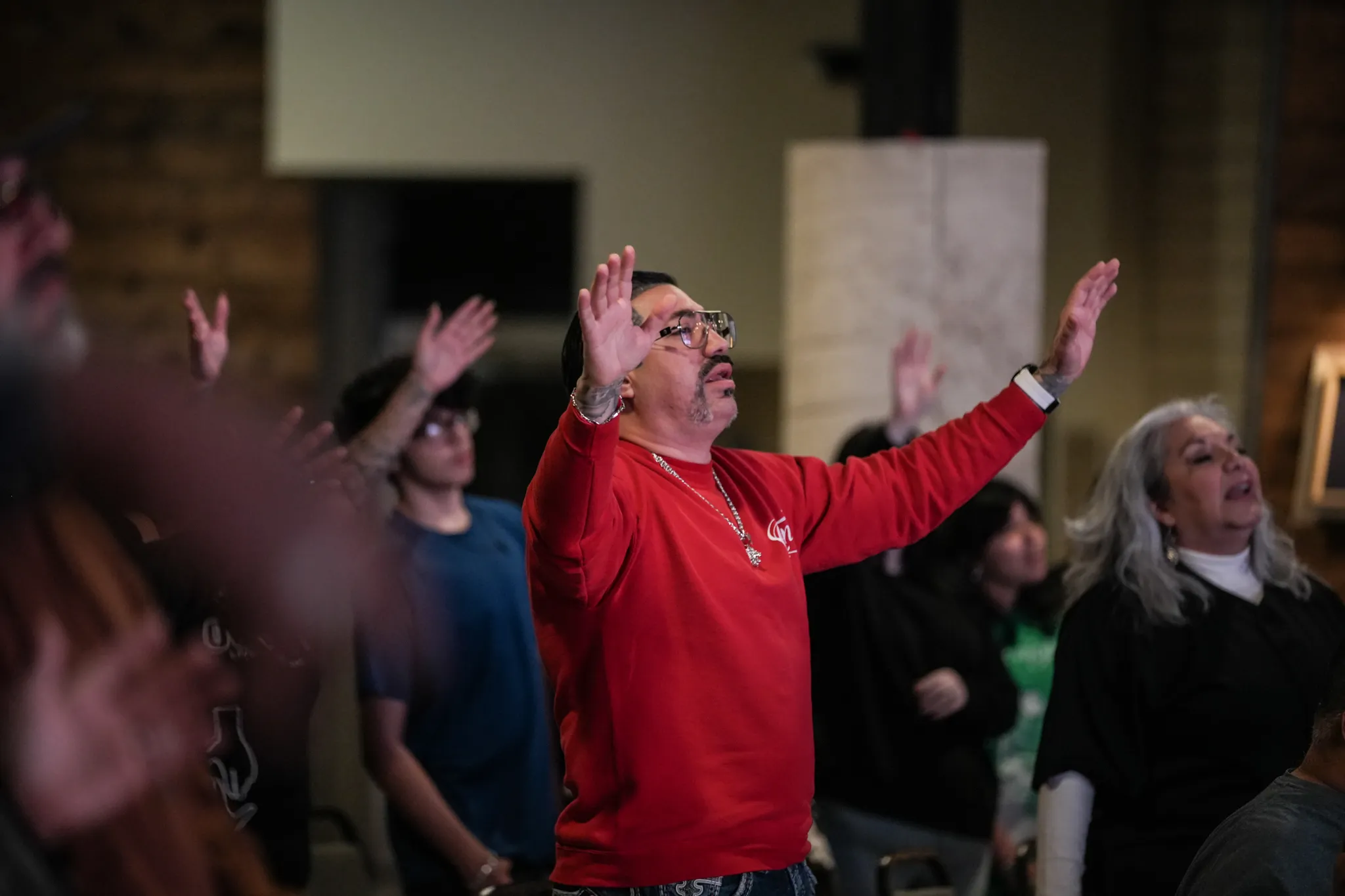 Man in red shirt raising hands in worship indoors