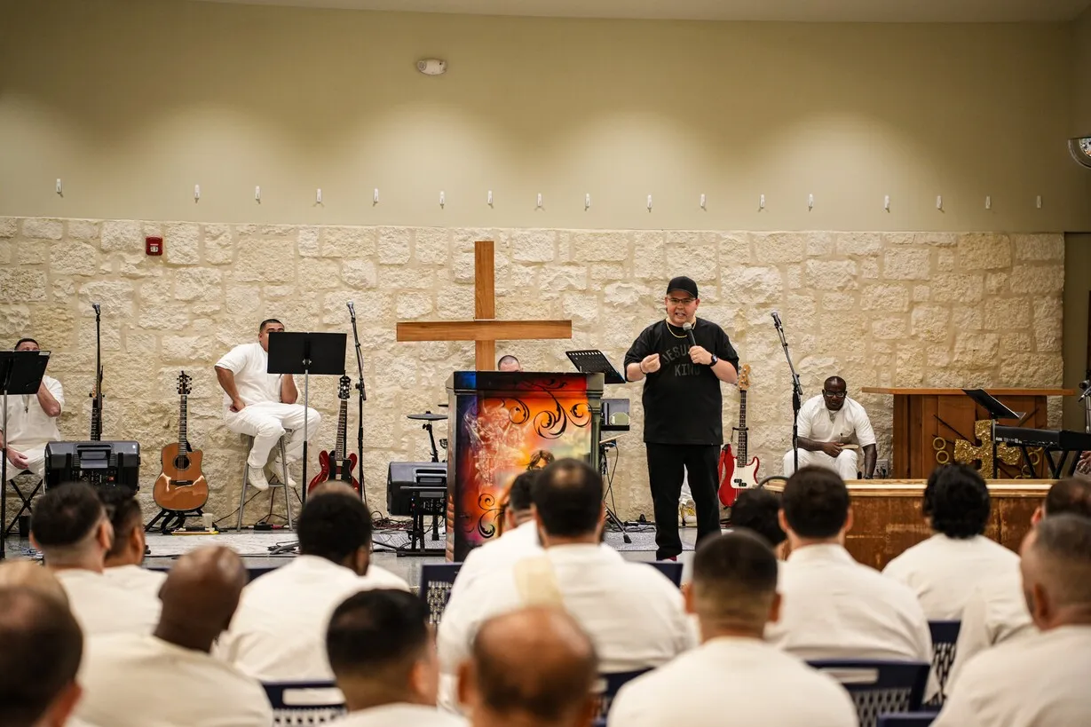 Pastor preaching to inmates in prison chapel with band