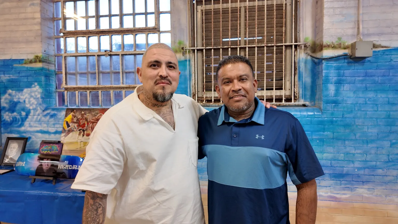 Two men smiling together in front of ocean mural