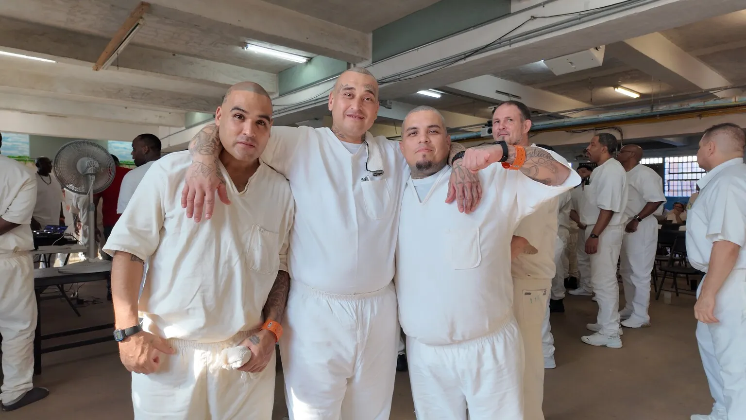Four inmates in white uniforms posing together in dining hall