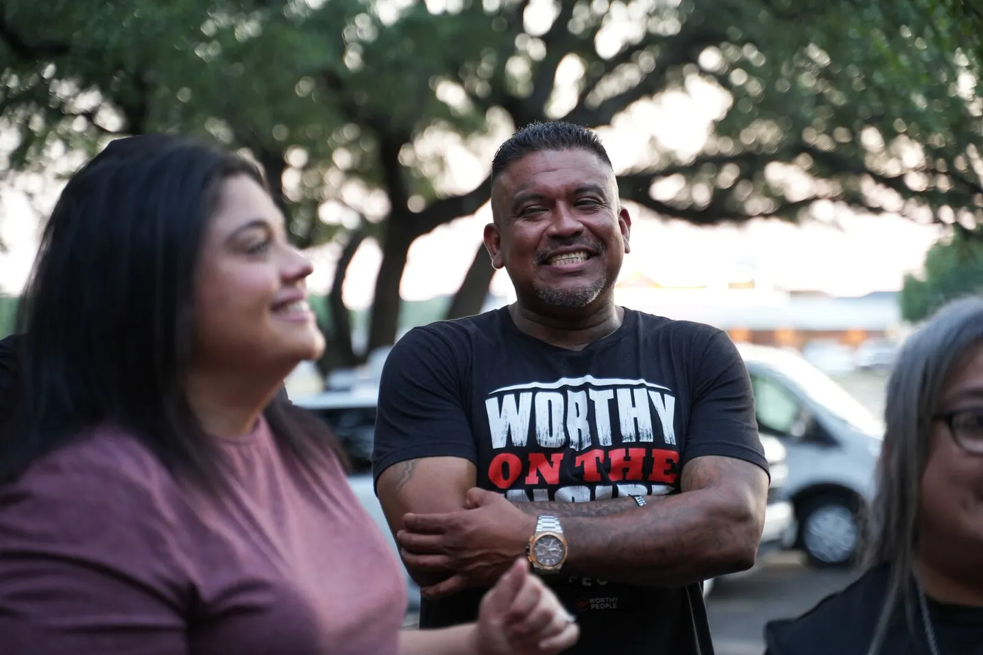 Man in Worthy People shirt smiling with two women outdoors