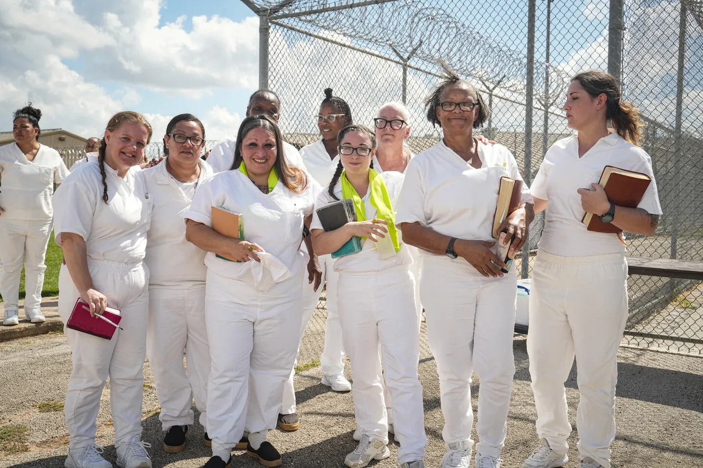 Group of women in white uniforms outside prison fence