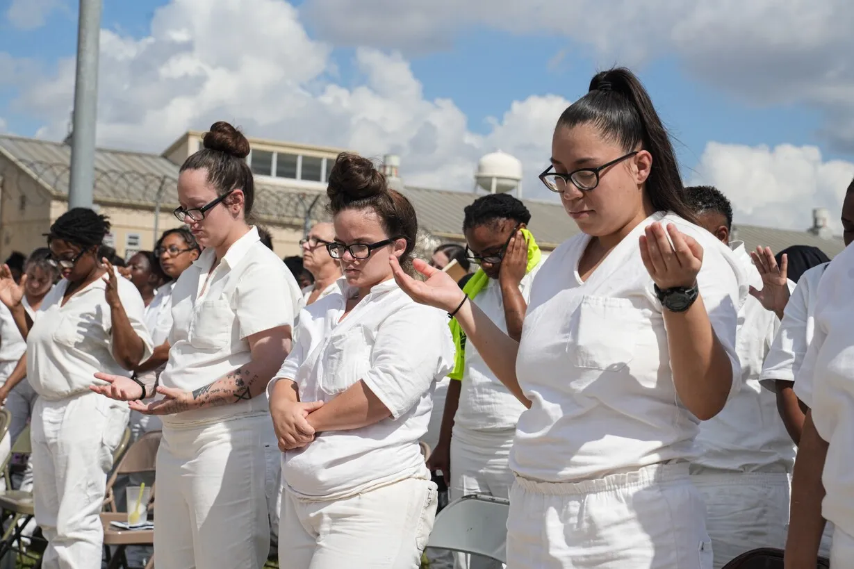 Women in white uniforms praying outdoors at prison ministry