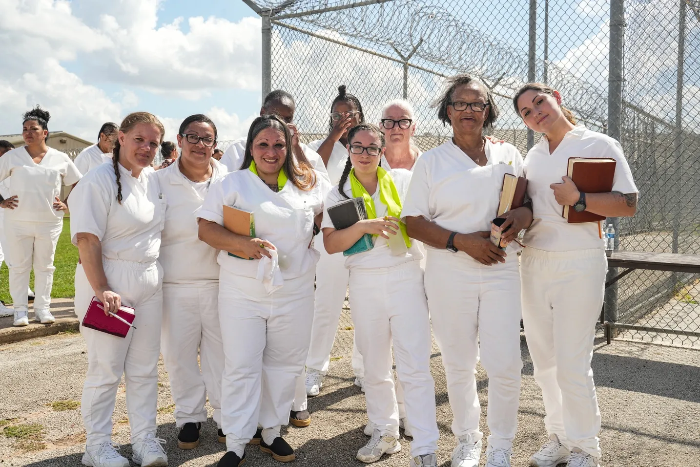 Women in white holding Bibles outside prison fence