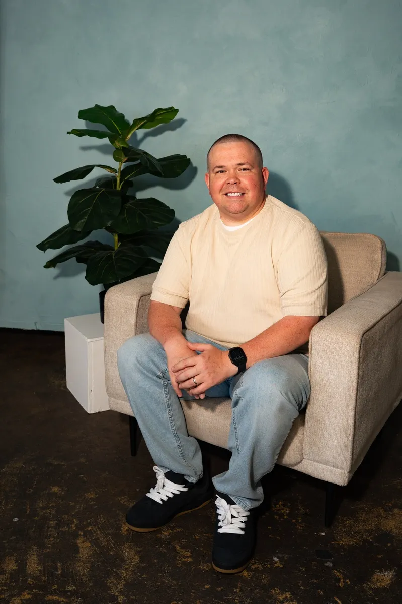 Man smiling seated in armchair beside potted plant