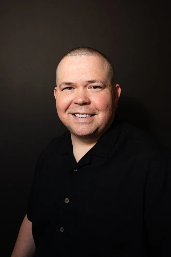Studio headshot portrait of man in black polo shirt