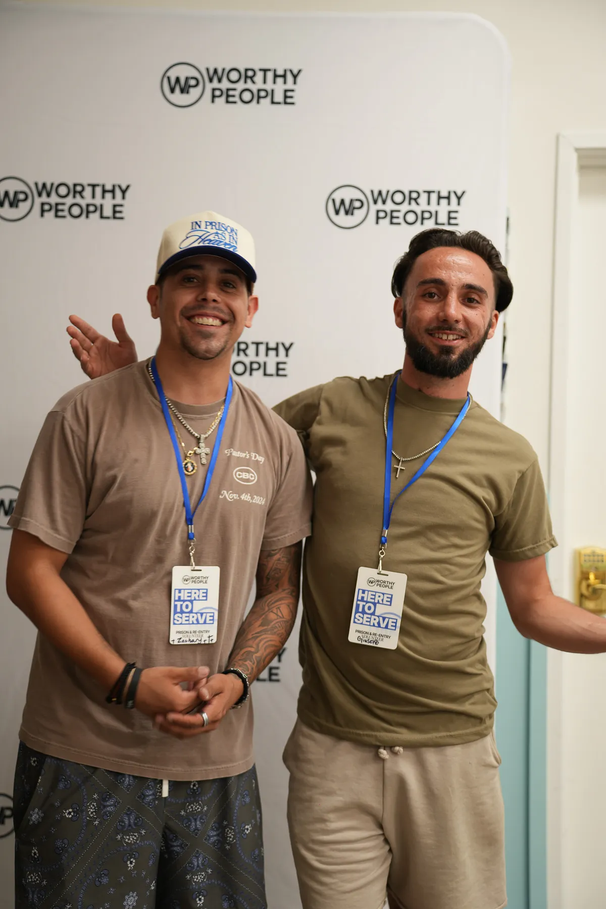 Two guests posing with Here to Serve lanyards