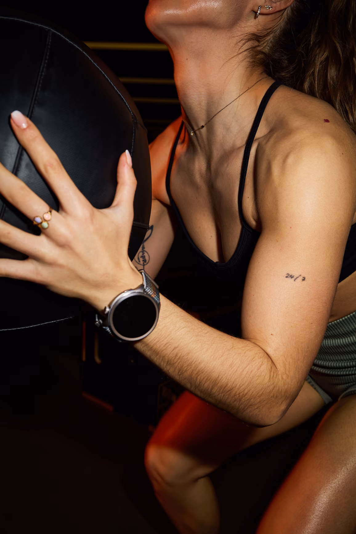 Close-up of a woman holding a black medicine ball while exercising in gym lighting.