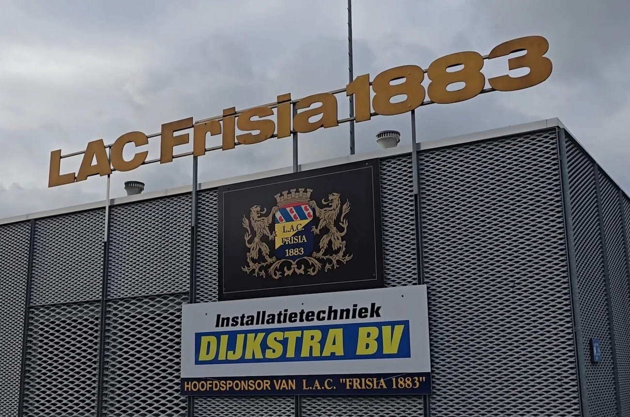 Buitengevel van L.A.C. Frisia 1883 met de clubnaam in gouden letters en het wapenschild, sponsorbord van Dijkstra BV eronder.