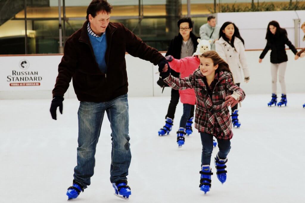 Sports parent ice skating with his daughter