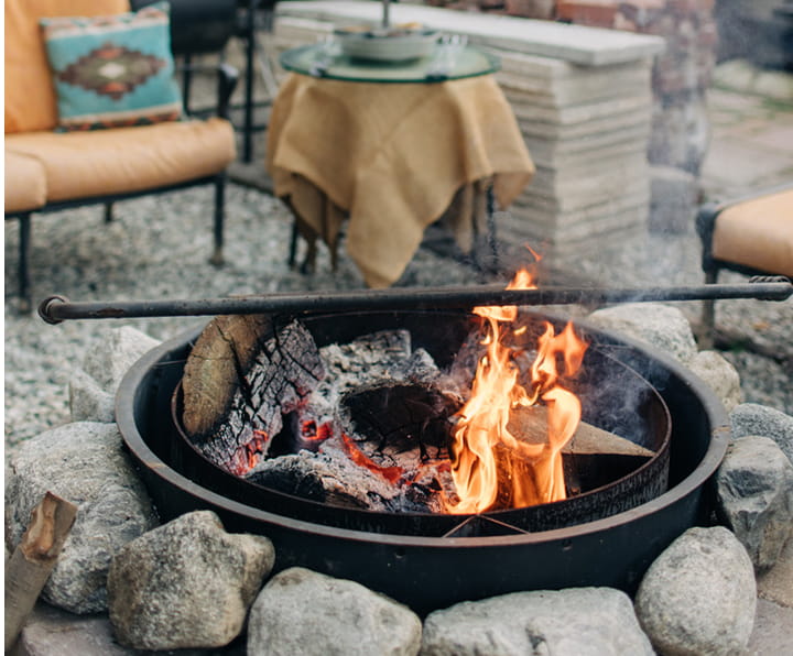 Outdoor fire pit with burning logs surrounded by large rocks in a patio seating area.