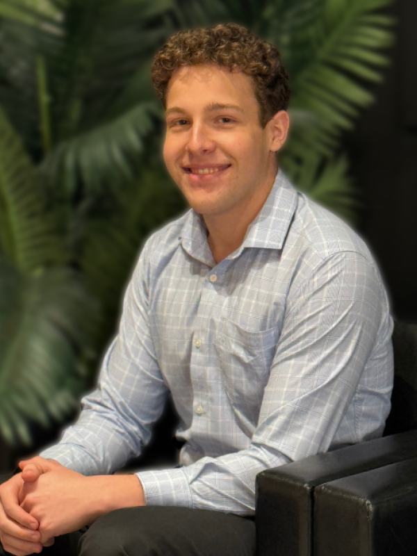 Thomash Zamin, Software Developer Intern sitting in a black chair with blurred black wall and green plant in the background