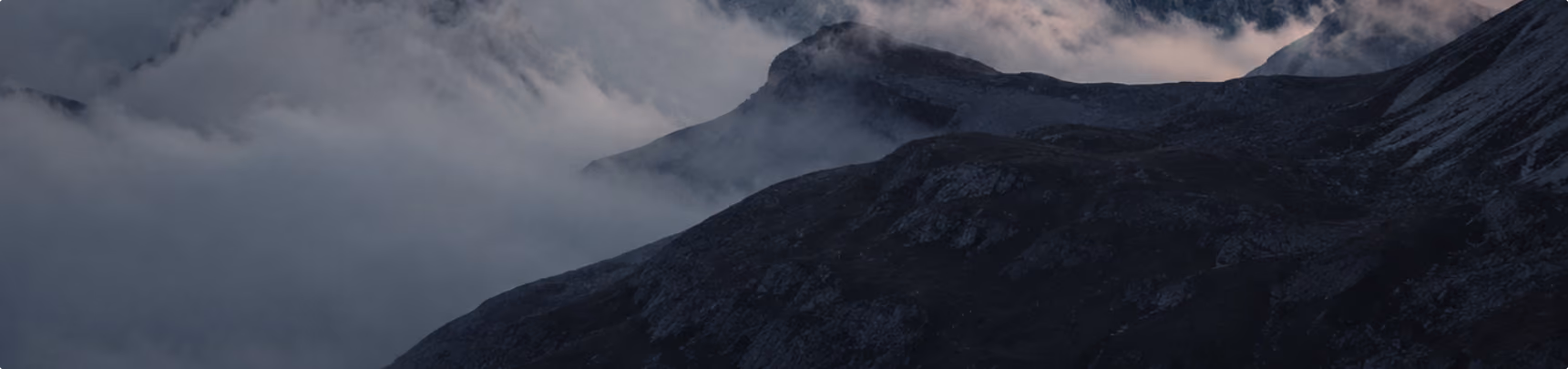 Mountain peaks shrouded in mist and clouds under a dark, moody sky.