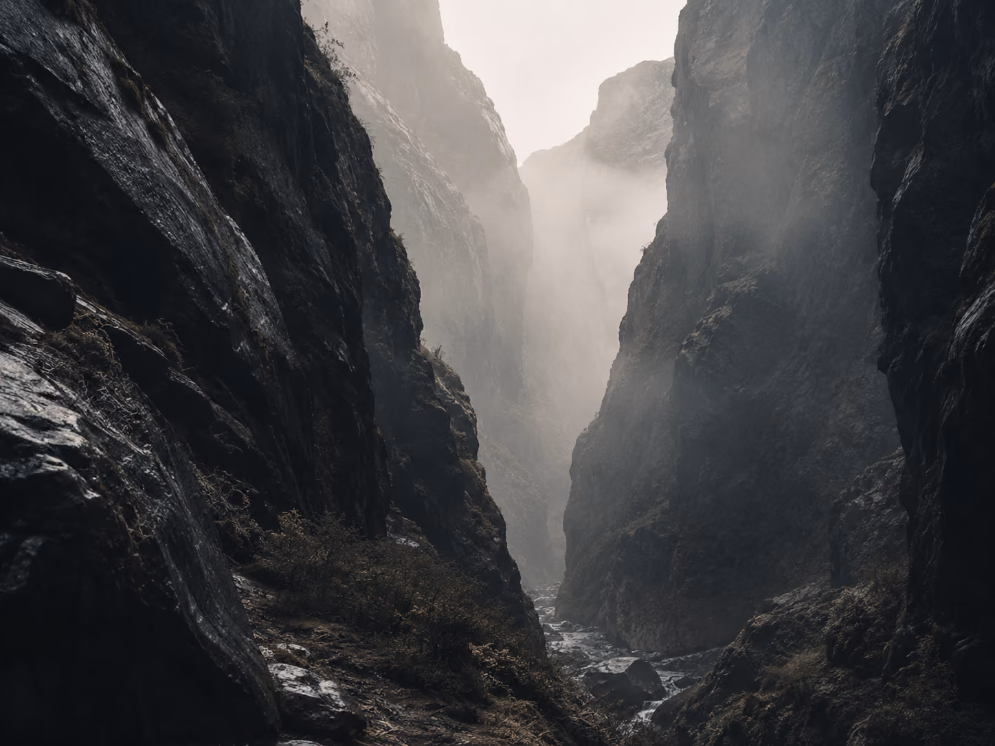 Narrow rocky canyon with mist and a small stream running through the bottom.